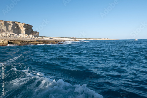 Open sea with rugged rocky coastline seen from a moving boat, featuring deep blue water, waves and raw Mediterranean coastal scenery suitable for travel and nature concepts.