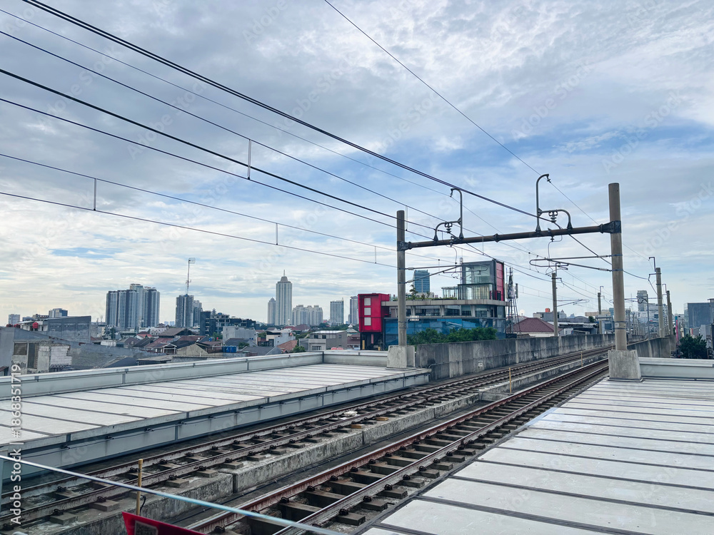 Fototapeta premium A wide-angle, high-angle view of elevated commuter railway tracks stretching into the distance towards a modern urban skyline.