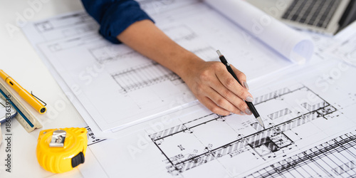 Foto Close up hand of Architect or engineer hand holding pen working on blueprint construction floor plans on desk with engineering tools