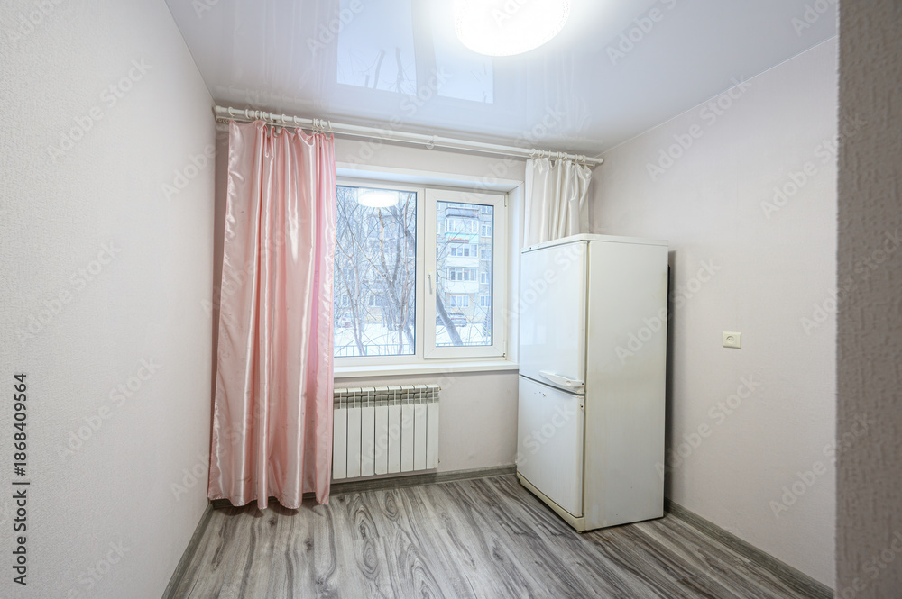 Fototapeta premium Small room with light grey laminate floor, white walls, double window with pink and white curtains, white radiator, white fridge, simple ceiling light