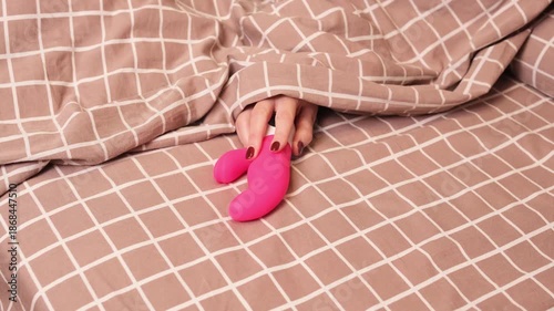 A womans hand reaches out from under the blanket for a vibrator. A woman takes an adult toy to satisfy herself.