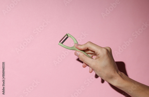 Photos Hand holding Kitchen peeler knife for peeling vegetable skins on pink background
