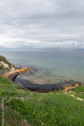 Minimal Mediterranean seascape with calm water and rocky shoreline beneath a cloudy sky, showing an open coastal view that conveys silence, balance and a strong connection with nature.