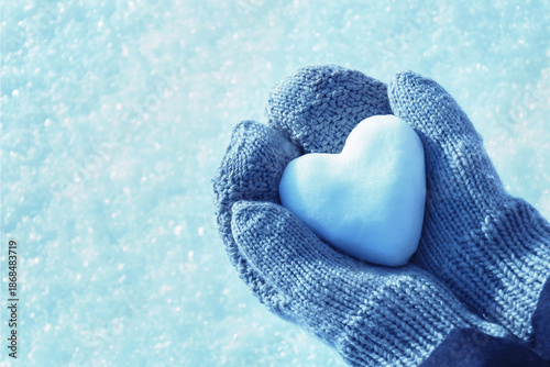 Hands in knitted mittens hold heart of snow in winter day. Love concept. Valentine day concept.	