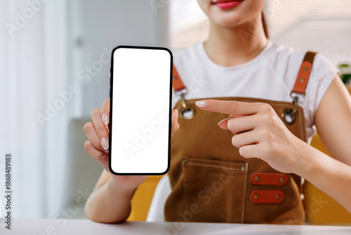 Φωτογραφία Hands of a woman in an apron holding a modern smartphone with a blank white scre