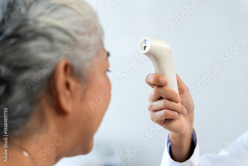 Photos Healthcare worker checking senior woman's temperature using a non contact infrar