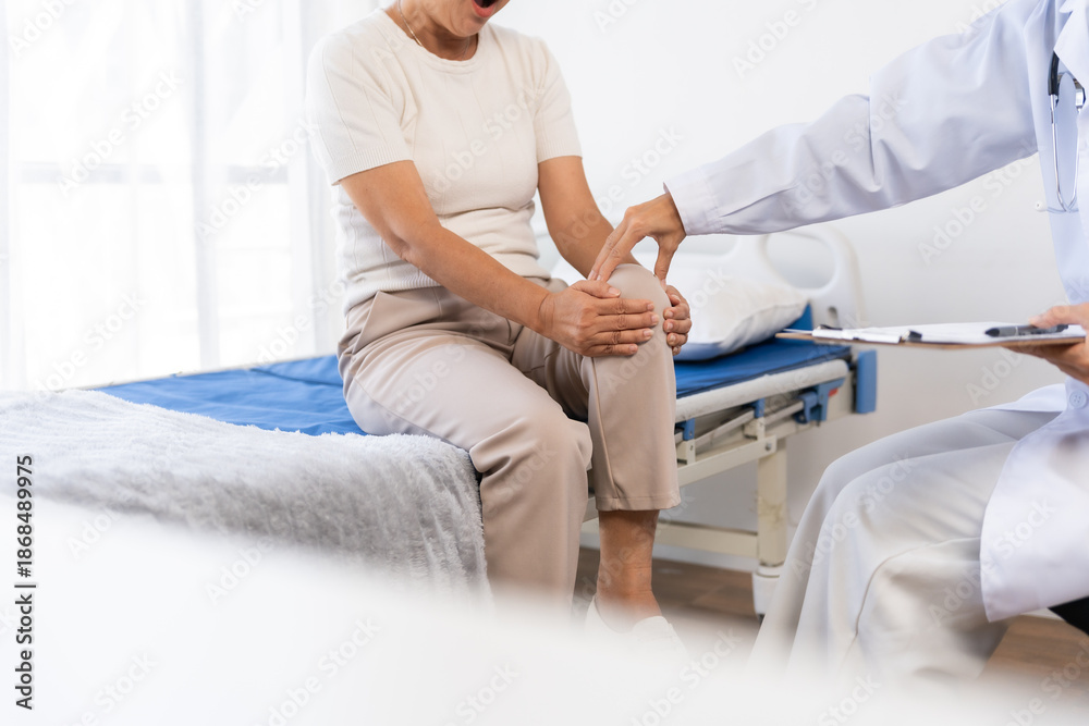 Obraz premium Doctor examining a senior woman's knee to diagnose joint pain. Healthcare professional providing care for an elderly patient