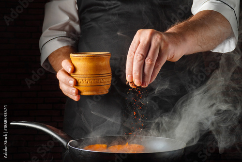 Fotografi A cook prepares in the kitchen, adding spices from a wooden bowl to a frying pan of simmering pumpkin on the stove