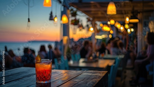 Sunset scene with a cocktail on a wooden table at an outdoor bar, blurred background