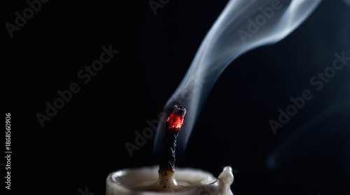 Extinguished candle with smoke trail and glowing red wick on black background. Biblical symbol of fragile faith and prayer. Spiritual concept of hope during Lent.