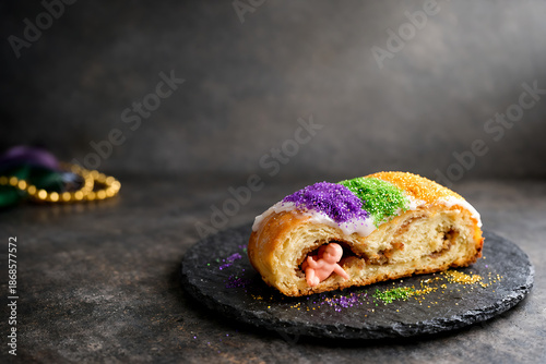Delicious King Cake with baby inside on black slate plate Mardi Gras celebration