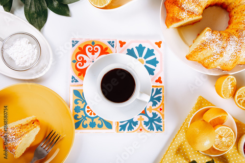A vibrant top-down view of a cozy coffee break featuring a cup of black coffee, powdered sugar-dusted cake slices, fresh lemons, and colorful patterned coasters on a bright, inviting table.