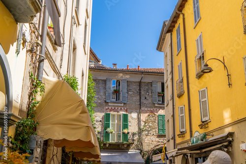 Multicolor windows balcony with shutters. Italy empty narrow street in summer day. Italian style facade architecture. House yellow wall in Como
