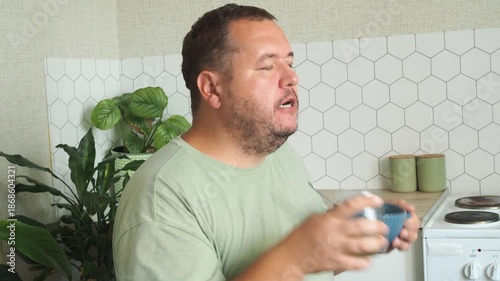 A fat man is drinking juice in his kitchen.