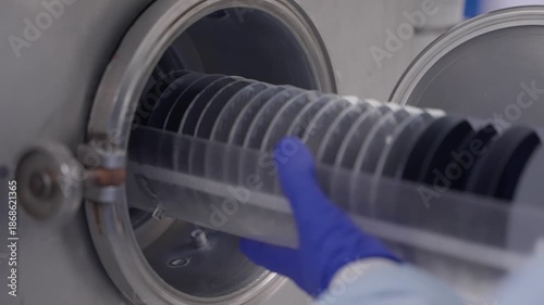 Cleanroom technician loading a silicon wafer cassette into a vacuum processing chamber with protective gloves, ensuring precision handling in a controlled environment.