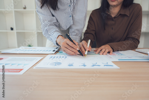Business Collaboration: Two female colleagues engrossed in a focused discussion, analyzing charts and diagrams during a business meeting, emphasizing teamwork and shared decision-making.