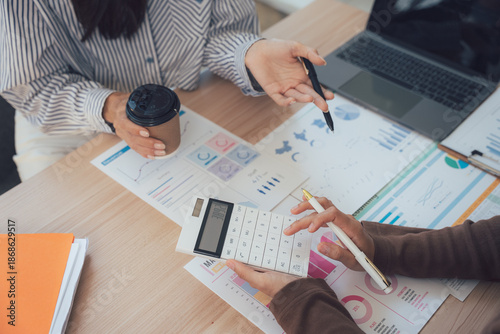 Obraz na plátně Financial Analysis Partnership: Two professionals deeply engaged in a dynamic partnership, working together to dissect complex financial data, with a laptop, calculator, and coffee