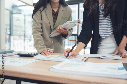 Fotografia Strategic Planning in the Office: A focused scene of two businesswomen deep in thought, collaborating around a desk laden with documents, as they analyze data and meticulously plan for future success