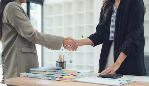 Business Deal Sealed with Handshake: Two women, dressed in professional attire, seal a deal with a firm handshake, symbolizing partnership and agreement. The focus is on the human interaction.