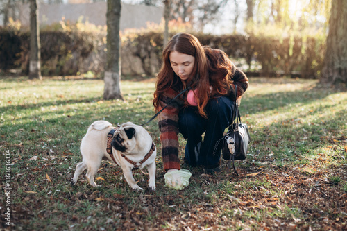 Woman picking up her dog's poop from grass in park.