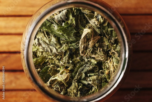 Photography Dried nettle leaves in glass jar viewed from above on wooden table