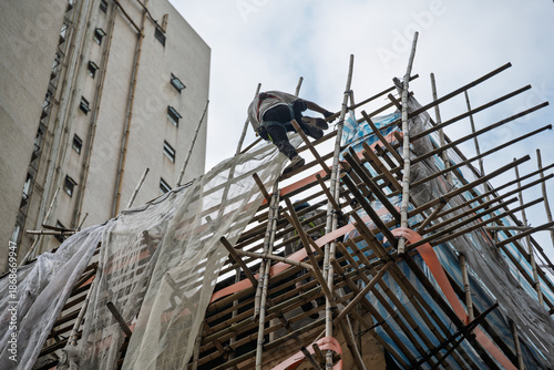 Hong Kong, China : construction worker climbing traditional bamboo scaffolding during building renovation in the city