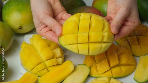 Hands showing and opening a fresh diced half of a mango fruit.