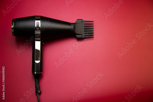 Close-up of a black hair dryer with a comb attachment to create volume on a pink background with space for text. The concept of long-term hair styling, hairstyles, curls and hair care. High quality