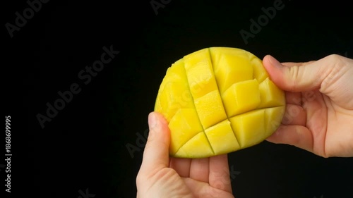 Hands showing and opening a fresh diced half of a mango fruit.