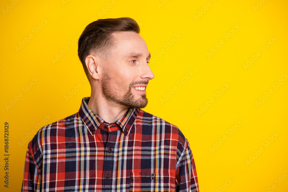 Fototapeta premium Young man in plaid shirt smiles as he looks aside against a bright yellow background for a casual fashion portrait suitable for advertising and lifestyle stock imagery