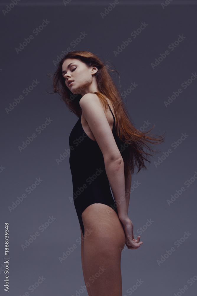 Fototapeta premium graceful woman in black bodysuit posing with closed eyes and flowing hair in studio setting