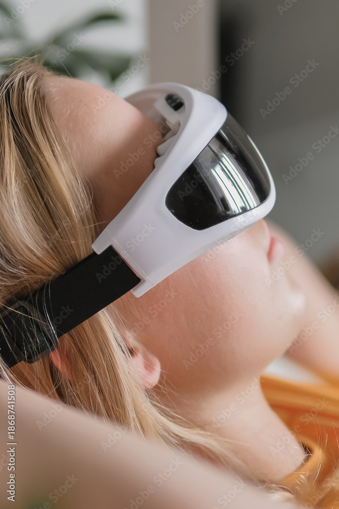 Fototapeta premium Gen Z woman unwinds home smart eye massagerЧwellness tech recovery, mindfulness and stress relief. Cozy greenery and soft light set a self-care, digital-detox mood, promoting balance, calm wellbeing