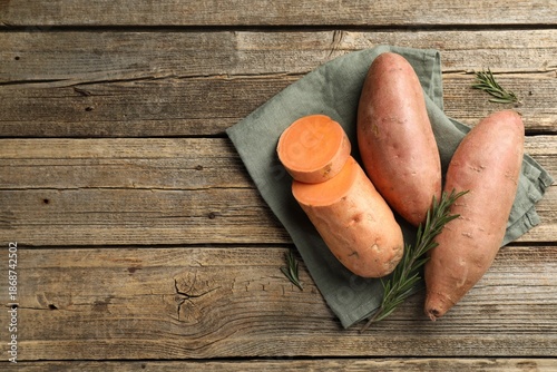 Raw sweet potatoes with rosemary on wooden table, flat lay. Space for text © New Africa
