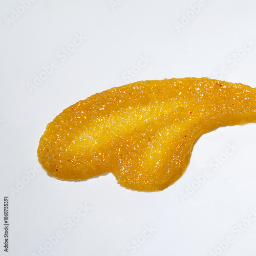 Smears of orange or yellow body scrub isolated on white, top view.