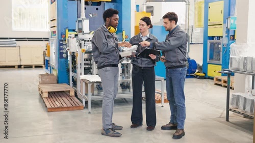 Team of factory workers in gray uniforms conducting quality control inspection. Manager demonstrating aluminum foil containers to colleagues. Discussing production details at manufacturing facility.