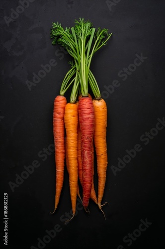 Fresh Carrots With Green Tops Placed on a Black Surface in Natural Light Duri...