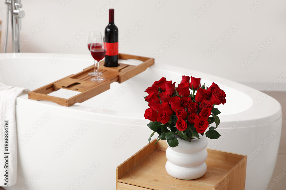 Fototapeta premium Vase with red roses on table in bathroom decorated for Valentine's Day