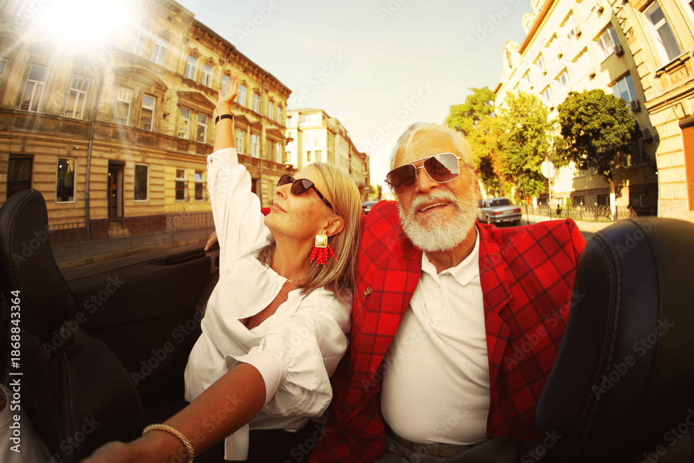 Fototapeta premium Stylish elderly couple enjoying ride in convertible car on sunny day, wide angle lens