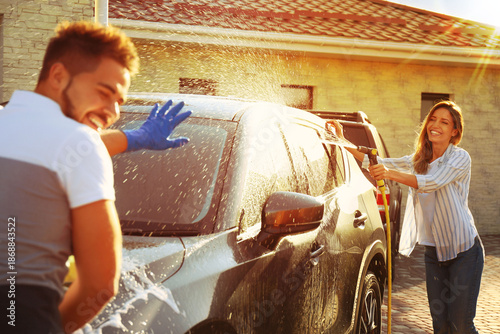 Schilderij op canvas Happy couple washing car and having fun at backyard on sunny day