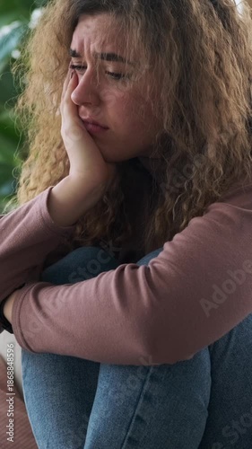 Vertical video of a sad and depressed young woman sitting alone at home, feeling hopeless, lonely, and anxious.