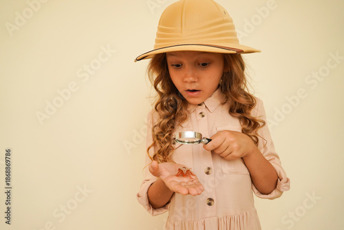 Child discoverer. Traveler child. Young entomolog. A little girl looks with interest through a magnifying glass at a large plastic fly sitting on her palm. Concept: search for adventure and treasure.	