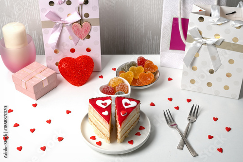 A dessert table features a slice of cake decorated with hearts, colorful candy, and wrapped gifts. Small hearts are scattered across the table. Items create a festive atmosphere..