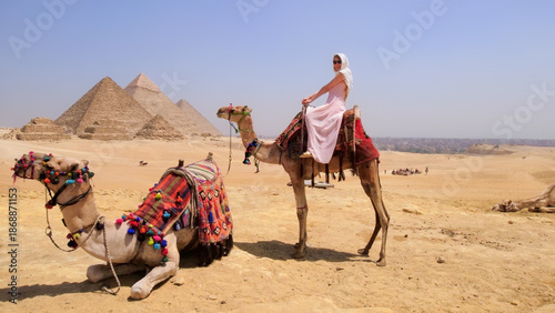 Tablou pe pânză A joyful traveler rides a camel in the Egyptian desert with the iconic Giza pyramids in the background, capturing the perfect vacation moment