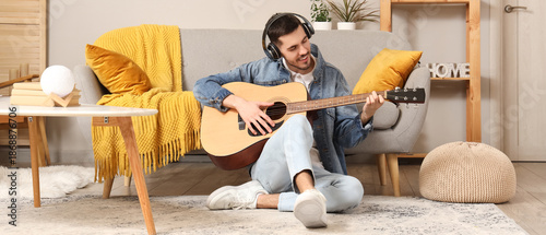 Young bearded man in headphones playing guitar at home
