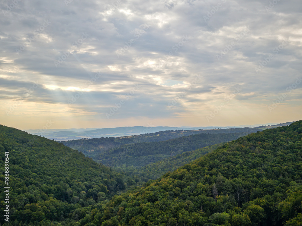 Naklejka premium Panoramic scenic view of green forested hills and valleys under a dramatic cloudy sky.