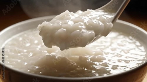 Steaming White Rice Porridge Congee or Bubur Scooped with Spoon in White Bowl with Soft Lighting and Warm Background