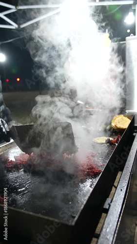 Slow-motion footage of al pastor pork grilling outdoors, with rising steam that emphasizes texture, heat, and authentic Mexican street food cooking - Taco Stand Series - Food vendor