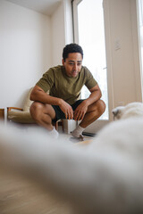 Candid moment: man crouching at home with curious cat nearby