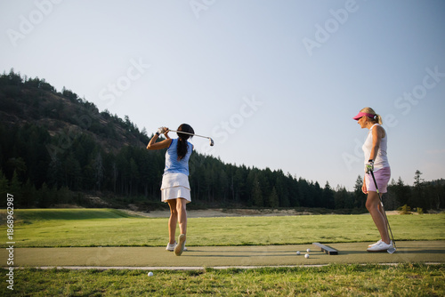 Women practicing golf on driving range with coach friend watching
