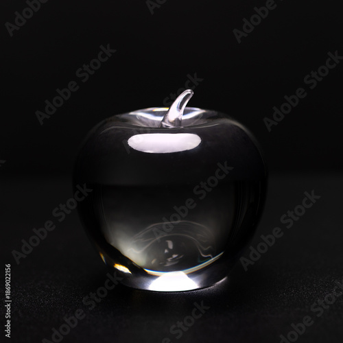 Canvas Print A clear glass apple paperweight sits on a black surface, illuminated by a light source that creates reflections and highlights on its surface